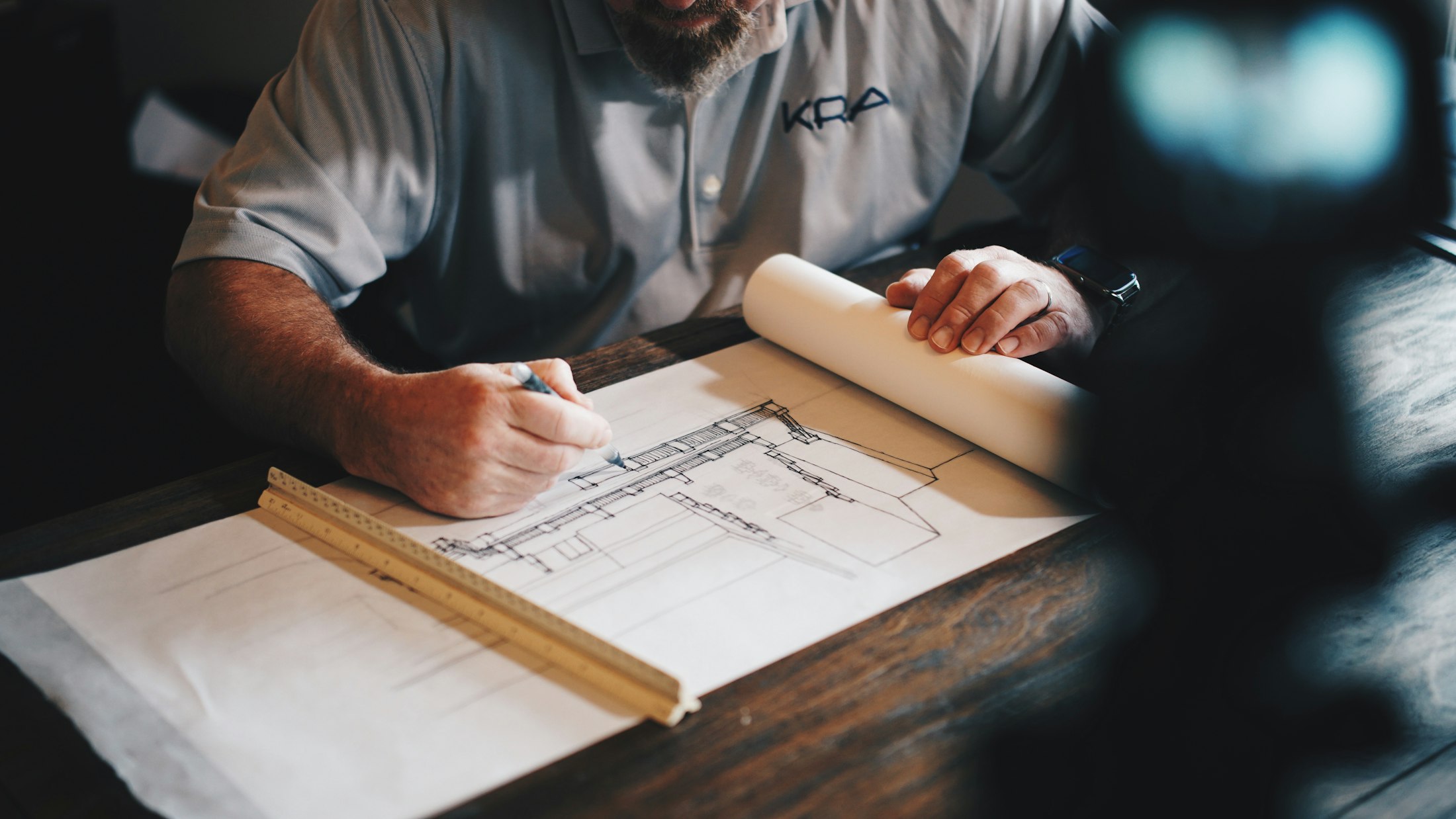 A builder marking up a construction drawing with a scale ruler